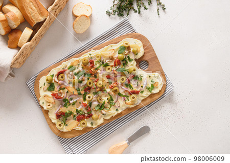 Homemade trendy butter board with onion, olives, herbs and bread. Butter board with toasts on dark background. 98006009