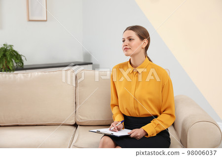 Professional psychotherapist with clipboard on sofa in office Professional psychotherapist with clipboard on sofa in office 98006037