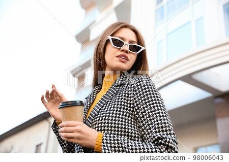 Young woman with cup of coffee on city street in morning Young woman with cup of coffee on city street in morning 98006043