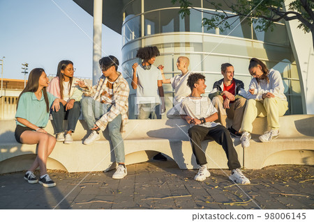 Big group of happy teenage friends talking in a bench in the street of the student campus. 98006145
