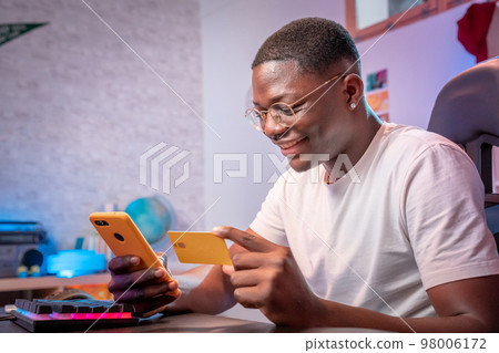 Young black man shopping online smiling happy holding mobile phone and credit card buy and pay 98006172