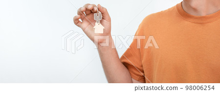 Banner of young man with the new home keys. Keychain in the shape of a wooden house. Banner of young man with the new home keys. Keychain in the shape of a wooden house. 98006254