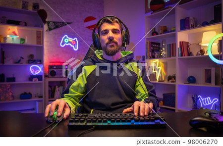 Happy gamer portrait playing games on the computer looking at camera while streaming gaming room. 98006270