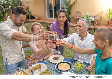 Friends toasting with beautiful smile around the table at house patio diner. Friends toasting with beautiful smile around the table at house patio diner. 98006368