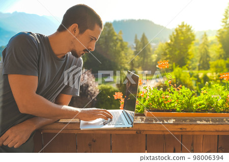 Young man working with laptop on beautiful scenic mountain background. Attractive man working. Freelancer. Traveler.  98006394
