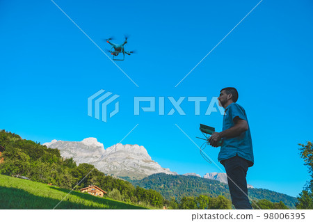 Young man flying drone on amazing mountain landscape. Man operating a drone with remote control taking aerial photos and videos. Young man flying drone on amazing mountain landscape. Man operating a drone with remote control taking aerial photos and videos. 98006395