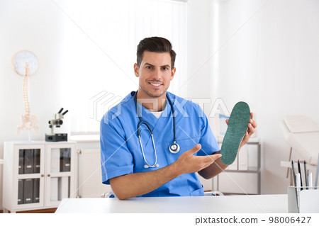Handsome male orthopedist showing insole in clinic Handsome male orthopedist showing insole in clinic 98006427