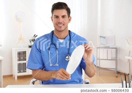 Handsome male orthopedist showing insole in clinic Handsome male orthopedist showing insole in clinic 98006430