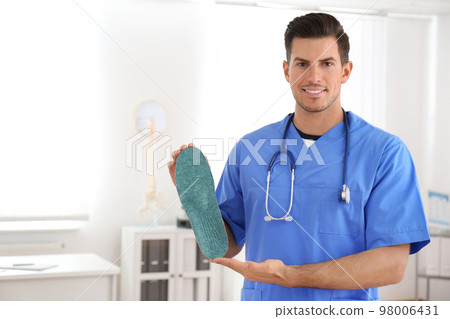 Handsome male orthopedist showing insole in clinic Handsome male orthopedist showing insole in clinic 98006431