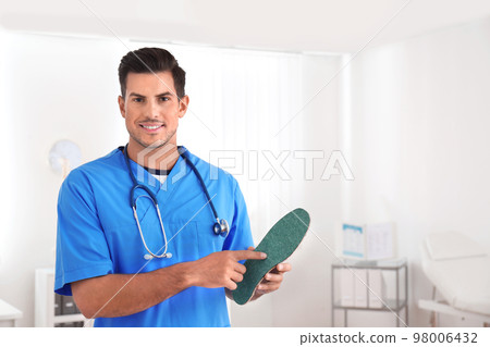 Handsome male orthopedist showing insole in clinic 98006432