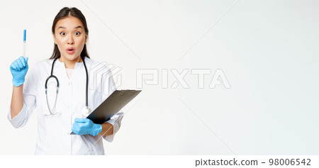 Enthusiastic nurse, asian woman doctor raising pen up, holding clipboard with patient papers, standing in uniform over white background Enthusiastic nurse, asian woman doctor raising pen up, holding clipboard with patient papers, standing in uniform over white background 98006542