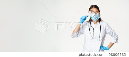 Asian female doctor looking through magnifying glass, examine patient, searching disease, wearing medical mask and rubber gloves, white background Asian female doctor looking through magnifying glass, examine patient, searching disease, wearing medical mask and rubber gloves, white background 98006583