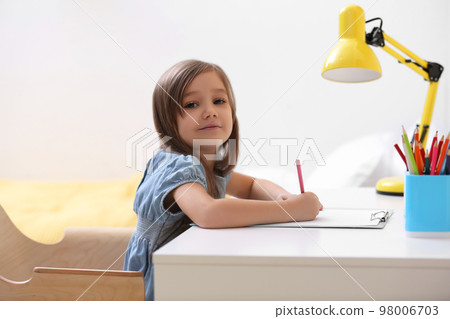 Cute little girl drawing at table in room 98006703