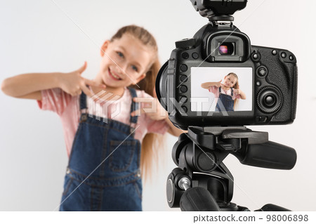 Cute little blogger recording video against white background, focus on camera 98006898