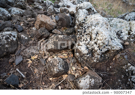 Closeup of large rocks or boulders near the mountains. Large multicolored granites. Details of big grey stone structures with orange particles shining in the sunlight. 98007347