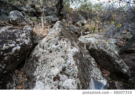 Closeup of large rocks or boulders near the mountains. Large multicolored granites. Details of big grey stone structures with orange particles shining in the sunlight. 98007359