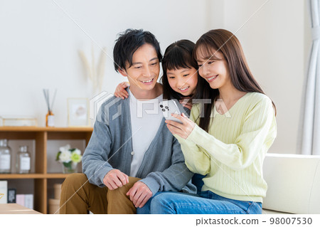 A young family looking at a smartphone in the living room A young family looking at a smartphone in the living room 98007530