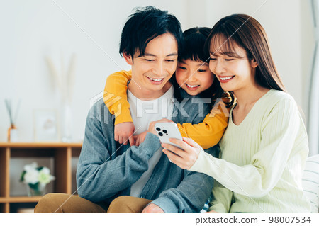 A young family looking at a smartphone in the living room 98007534
