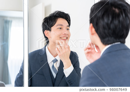 A businessman who checks his teeth by looking at the mirror (whitening, teeth alignment, orthodontics) A businessman who checks his teeth by looking at the mirror (whitening, teeth alignment, orthodontics) 98007649