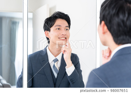 A businessman who checks his teeth by looking at the mirror (whitening, teeth alignment, orthodontics) A businessman who checks his teeth by looking at the mirror (whitening, teeth alignment, orthodontics) 98007651