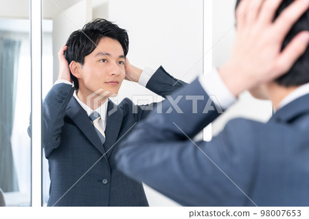 一個年輕的商人看著洗手間的鏡子，整理頭髮（頭髮，早上，準備工作） 98007653