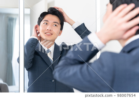 一個年輕的商人看著洗手間的鏡子,整理頭髮(頭髮,早上,準備工作) 一個年輕的商人看著洗手間的鏡子,整理頭髮(頭髮,早上,準備工作) 98007654