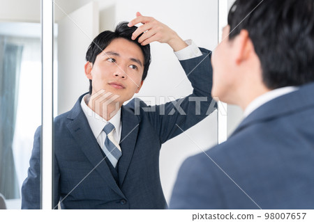 A young businessman looking at the mirror in the washroom and setting his hair (hair, morning, preparation for work) 98007657