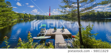 Two Ontario chairs sitting on a wood dock facing a calm lake. Two Ontario chairs sitting on a wood dock facing a calm lake. 98011829
