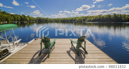 Two Ontario chairs sitting on a wood dock facing a calm lake. Two Ontario chairs sitting on a wood dock facing a calm lake. 98011832