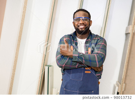 Short black hair man with moustache and beard stand with arm folded, smiling and raise finger thumb up. Plywood storage compartment are on the background. Carpenter worker work in a furniture factory. Short black hair man with moustache and beard stand with arm folded, smiling and raise finger thumb up. Plywood storage compartment are on the background. Carpenter worker work in a furniture factory. 98013732