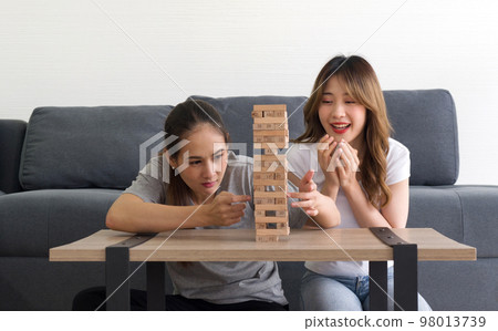 Two asian woman enjoy playing wooden blocks game in the living room. Players take turns removing one block at a time from a tower constructed of 54 blocks. Two asian woman enjoy playing wooden blocks game in the living room. Players take turns removing one block at a time from a tower constructed of 54 blocks. 98013739