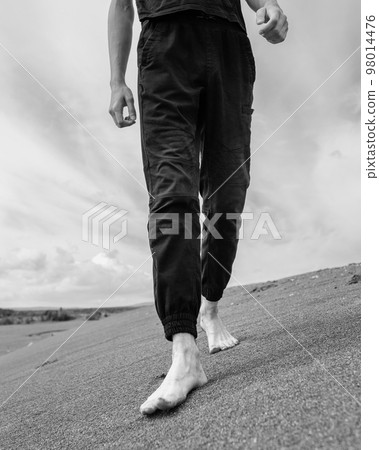 Young man walking alone on the sand in sandy desert Young man walking alone on the sand in sandy desert 98014476