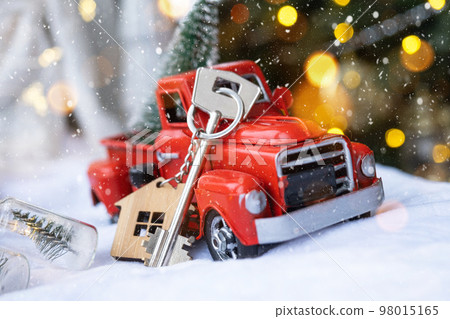 Red retro car with a Christmas tree decorates with the house key in the pickup truck for Christmas. Buying a home, moving, mortgage, loan, real estate, festive mood, New Year 98015165