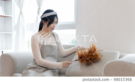 Housewife holding a dusting brush to clean things Pillows, rugs and other things in the living room, Big cleaning, Daily routine ,Removes germs and dirt and deep stains, Spray alcohol. 98015368