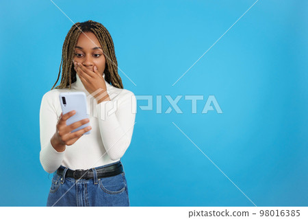 African woman looking at mobile phone with expression of surprise African woman looking at mobile phone with expression of surprise 98016385