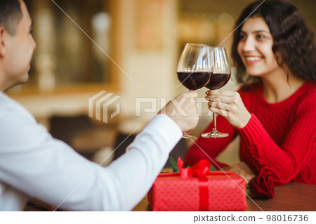 Couple clink glasses with red wine. Lovers give each other gifts. Lovely romantic dinner. 98016736