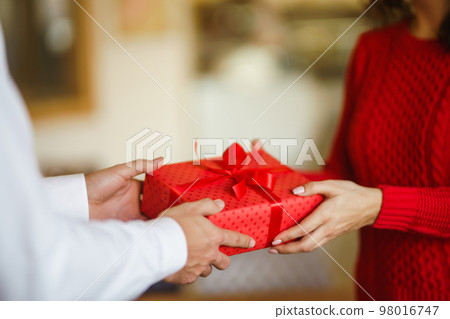 Man gives to his woman a gift box with red ribbon. Valentine's Day, holiday and surprise concept. 98016747