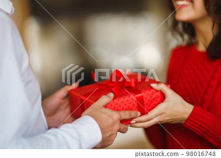 Man gives to his woman a gift box with red ribbon. A loving couple cuddles. 98016748