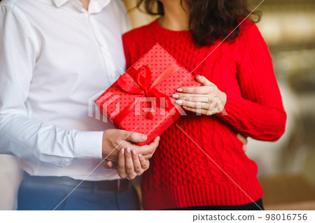 Man gives to his woman a gift box with red ribbon. Valentine's Day, holiday and surprise concept. Man gives to his woman a gift box with red ribbon. Valentine's Day, holiday and surprise concept. 98016756