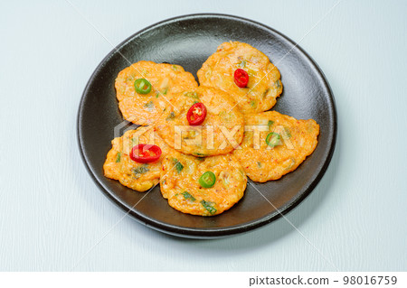 Korean traditional food kimchi jeon dish served with red and green chillies on a black plate Korean traditional food kimchi jeon dish served with red and green chillies on a black plate 98016759