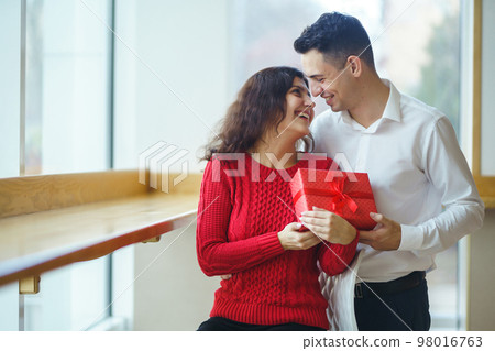 Man gives to his woman a gift box with red ribbon. A loving couple celebrating Valentine's Day. 98016763