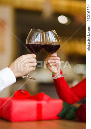 Couple clink glasses with red wine. Lovers give each other gifts. Lovely romantic dinner. Couple clink glasses with red wine. Lovers give each other gifts. Lovely romantic dinner. 98016794