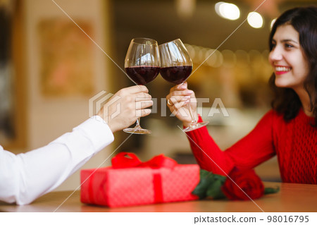 Couple clink glasses with red wine. Lovers give each other gifts. Lovely romantic dinner. Couple clink glasses with red wine. Lovers give each other gifts. Lovely romantic dinner. 98016795