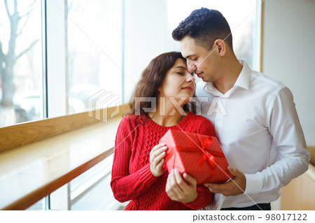 Man gives to his woman a gift box with red ribbon. A loving couple celebrating Valentine's Day. 98017122