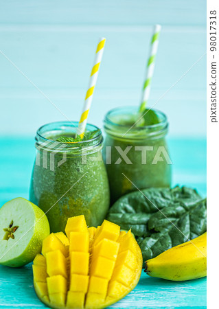 Freshly blended green smoothie with mango, apple and banana in glass jars. Turquoise blue background Freshly blended green smoothie with mango, apple and banana in glass jars. Turquoise blue background 98017318