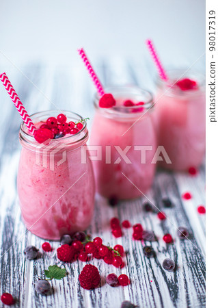 Front view of three berries milkshakes in glasses jars with ingredients on wooden table Front view of three berries milkshakes in glasses jars with ingredients on wooden table 98017319