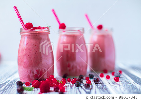 Front view of three berries milkshakes in glasses jars with ingredients on wooden background 98017343
