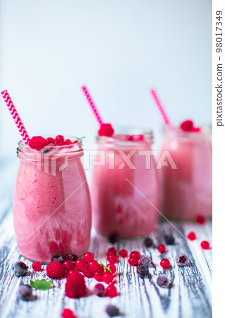 Front view of three berries milkshakes in glasses jars with ingredients on wooden table  98017349