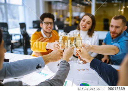 Clinking glasses with champagne. Happy coworkers celebrating their business achievement. 98017889