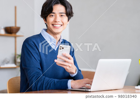 一個年輕人通過遠程辦公看智能手機 一個年輕人通過遠程辦公看智能手機 98018340